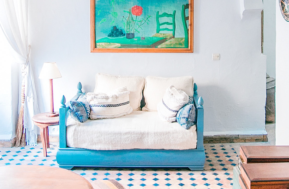 A medium blue daybed with white linens and throw pillows sits in a bright and airy room.